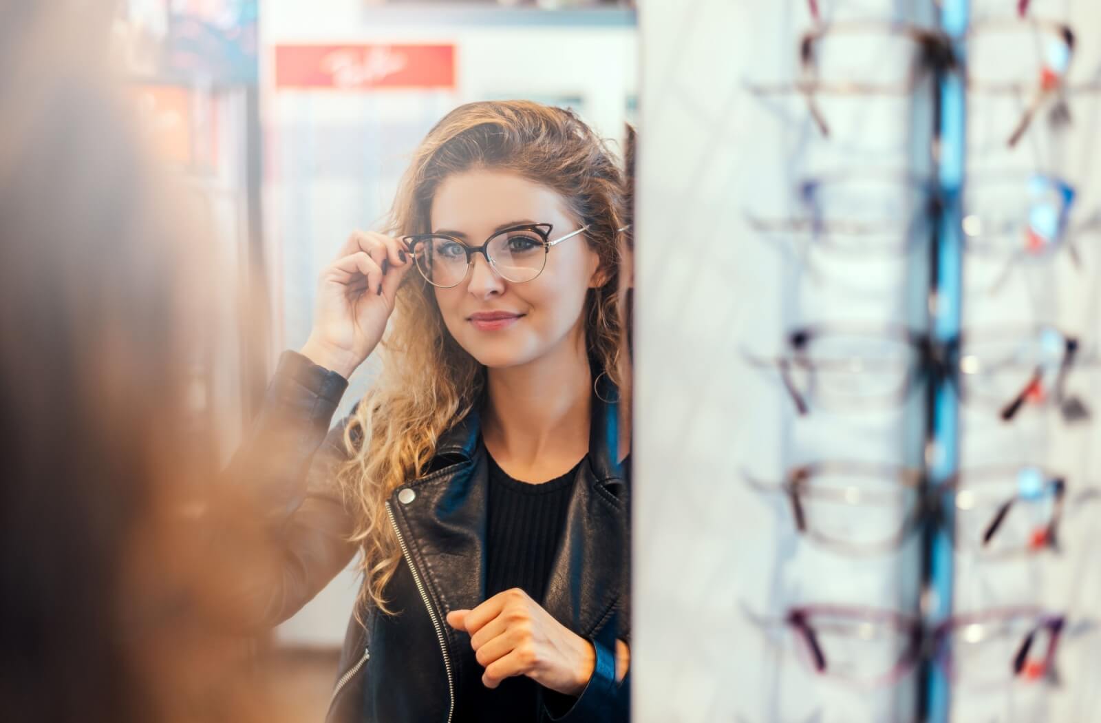 A young adult trying on a pair of cats-eye glasses in a mirror after their eye exam.