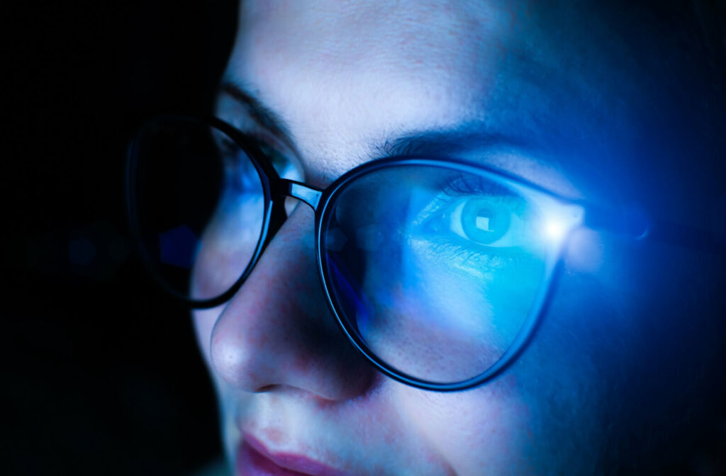 Close-up of a woman with blue light reflected on her glasses from a screen