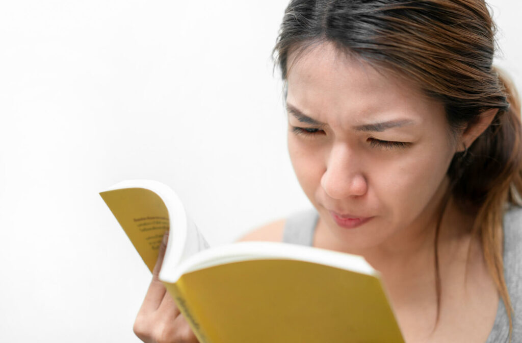 A woman having trouble reading a book and squinting to see better.