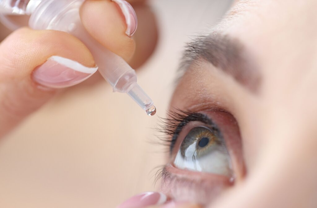 A close-up of a woman holding a bottle of eye drops and putting eye drops in her right eye