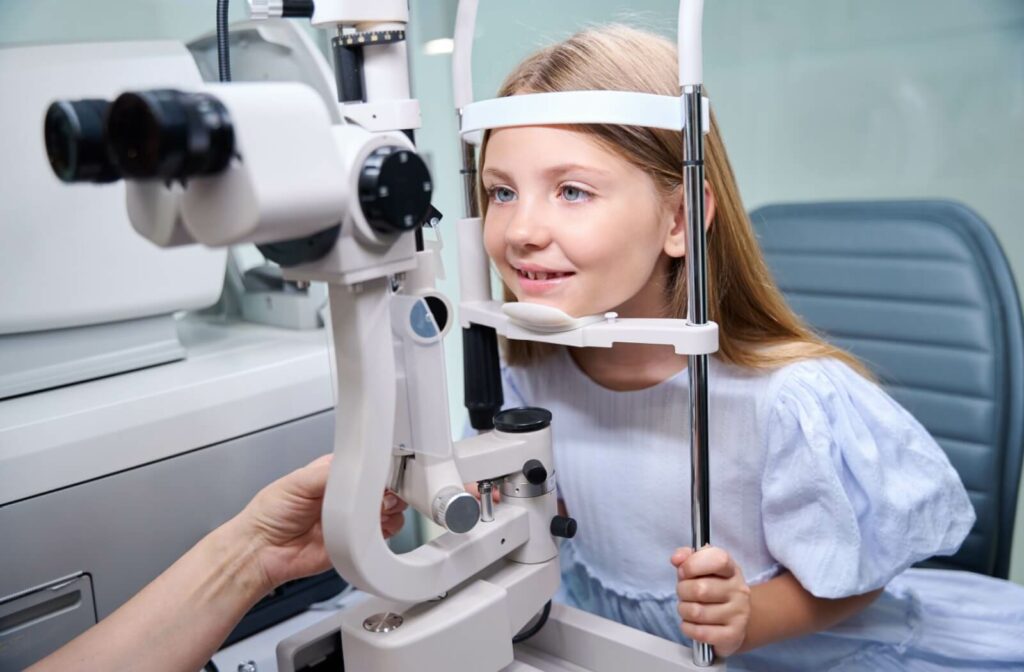 A young girl smiling while getting checked for myopia during a routine children's eye exam.