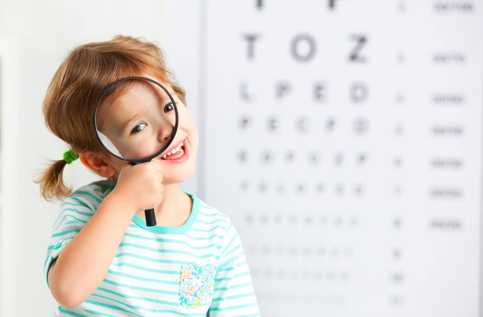 A child holds up a magnifying glass to their face in an optometrist's office.