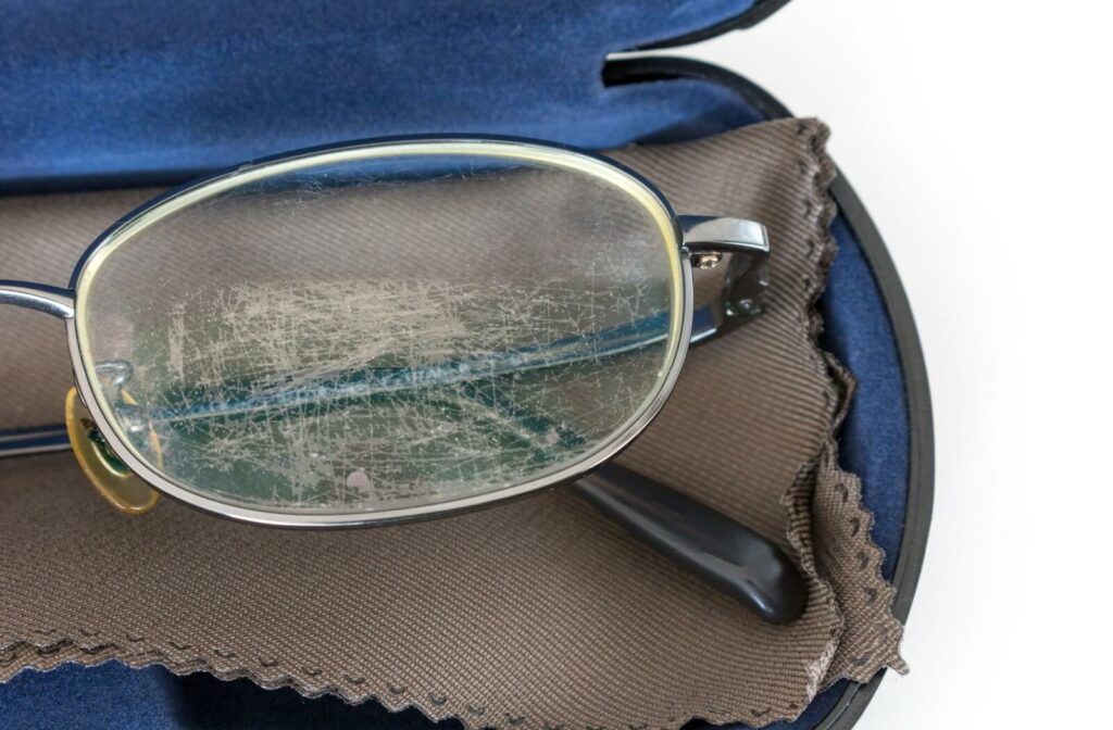 A pair of eyeglasses in their case shows signs of severe scratches and wear on their lenses.