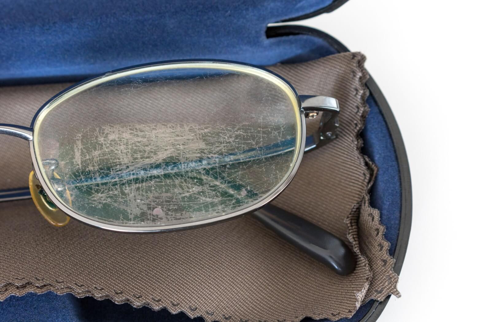A pair of eyeglasses in their case shows signs of severe scratches and wear on their lenses.