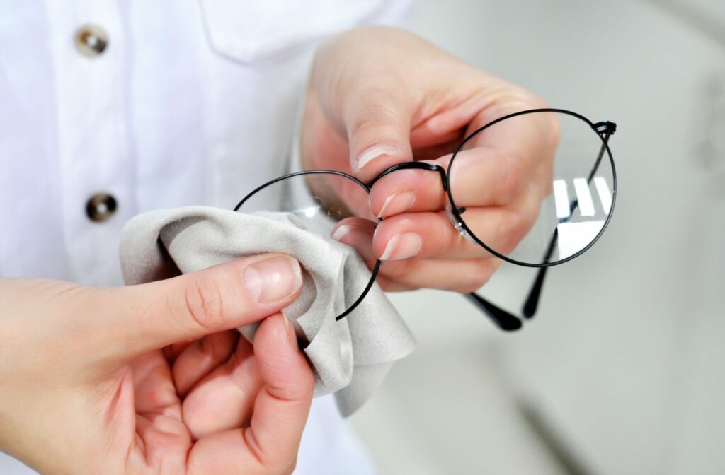 A person carefully cleans their eyeglasses with a microfibre cloth.
