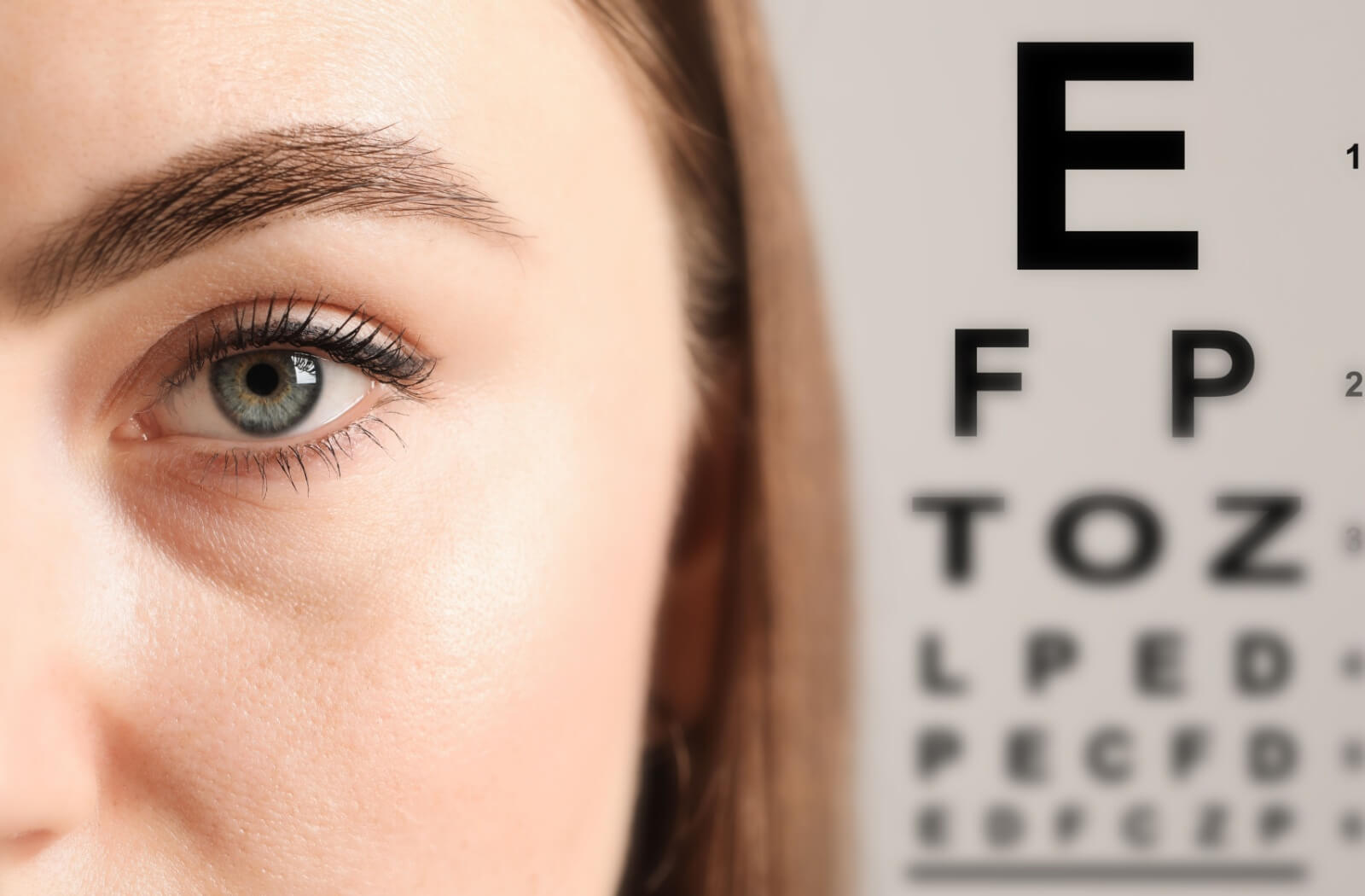 Close-up of a woman’s eye during an eye exam, with a Snellen vision chart visible in the background.