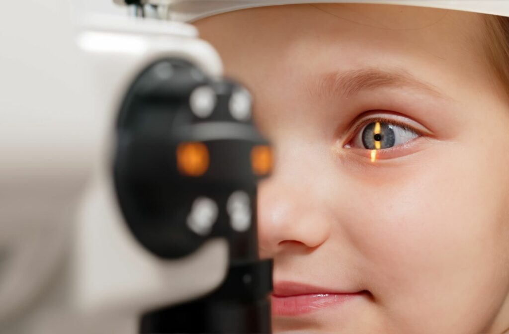 Close-up of a young child undergoing an eye exam with a slit lamp, showing a narrow beam of light illuminating the child’s eye as they look into the diagnostic device.