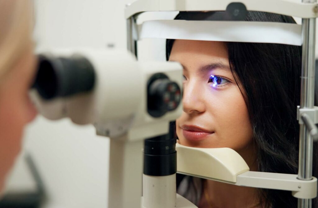 Person sitting at a slit-lamp exam machine while an eye care professional shines a blue light to examine the front of the eye.