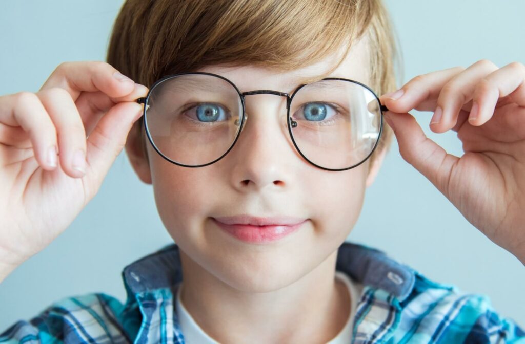 A child smiling while holding a pair of circular eyeglass frames.