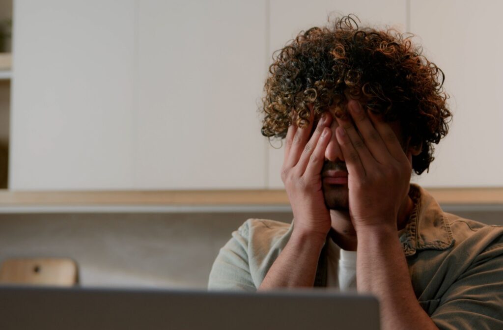 Covering eyes with both hands while working in front of a computer.